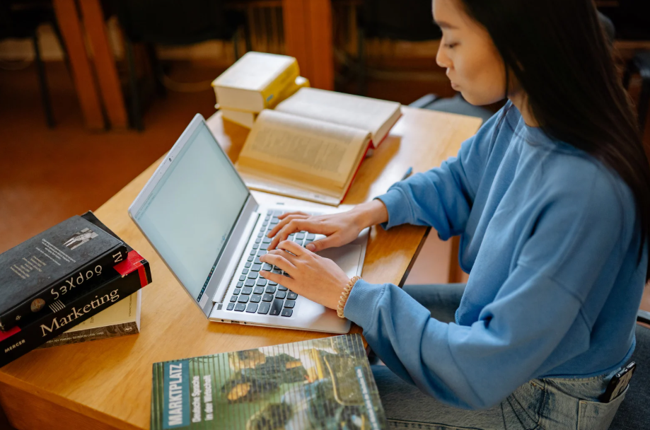 student studying business and technology degree programs using laptop and marketing textbooks